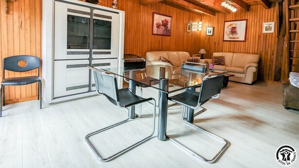 A wooden-paneled room with a glass dining table, two sofas, and a cabinet.