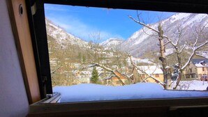 A snowy mountain landscape through a window with bare trees and buildings in the valley below.
