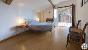 A bedroom with a bed, bedside lamps, a wooden chair, and a view of a wooden deck through a glass door. - Panifous - Montbrun-Bocage (Montbrun-Bocage)