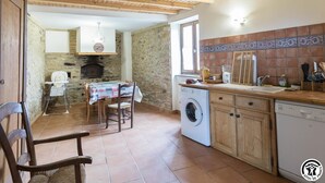 A kitchen with a washing machine, wooden cabinets, and a tiled backsplash. - Panifous - Montbrun-Bocage (Montbrun-Bocage)