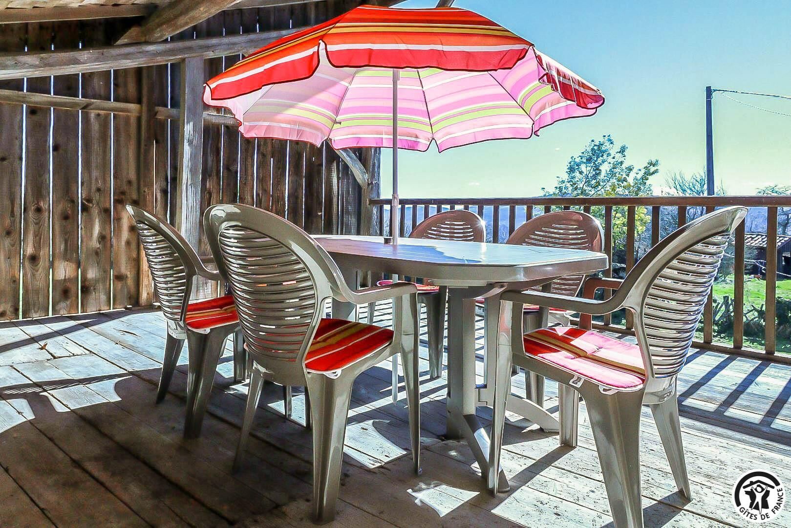 Een houten terras met een tafel, stoelen en een parasol, met uitzicht op de omgeving.