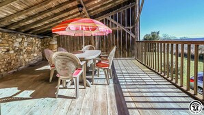 A wooden deck with a table and chairs under a striped umbrella, a stone wall, and a wooden railing overlooking a grassy area. - Panifous - Montbrun-Bocage (Montbrun-Bocage)