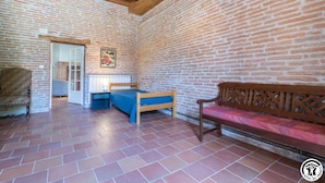 A room with a brick wall, a bed with a blue mattress, a wooden bench, and a chair.