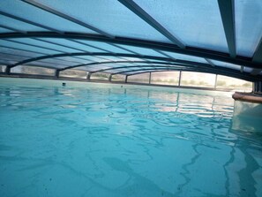 Une piscine intérieure à l’eau d’un bleu limpide, entourée d’une zone abritée dotée d’une structure de toit en métal.