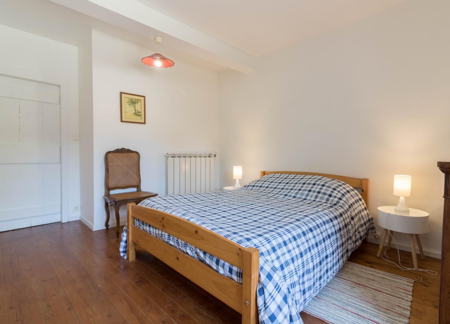 A bedroom with a wooden bed, a chair, a radiator, a lamp, and a small table.