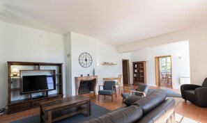 Ein Wohnzimmer mit Fernseher, Kamin, Sofa, Sesseln und Bücherregal.