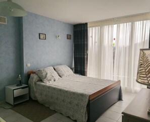 A bedroom with a bed, a nightstand, a lamp, and a window with curtains. - Arriehouat - Garin - Gîte (Garin)