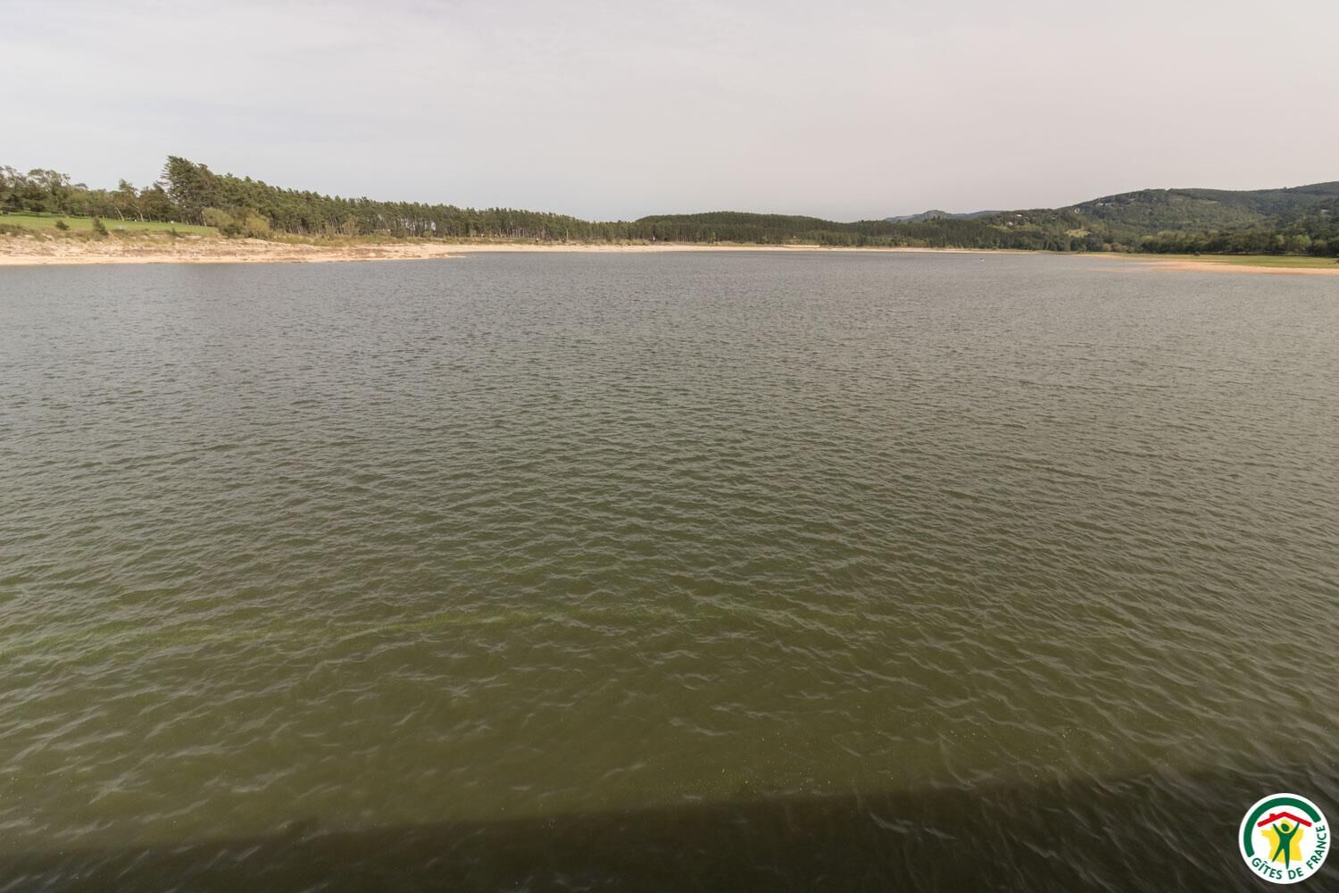 Tyyni järvi, jonka rannalla on hiekkaranta ja taustalla metsäinen kukkula.