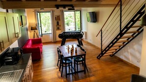 Une pièce chaleureuse avec un canapé rouge, une table à manger et des chaises, un baby-foot et un escalier.