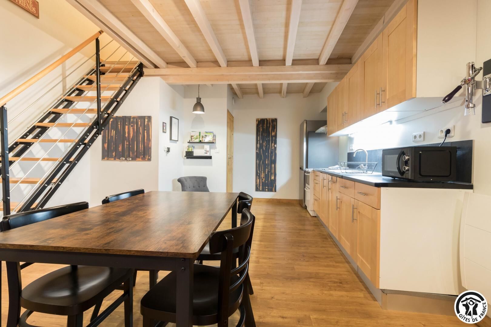 Une cuisine moderne avec des meubles en bois, un micro-ondes noir et un escalier doté d’une rampe en métal.