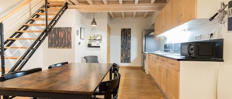 Une cuisine moderne avec des meubles en bois, un micro-ondes noir et un escalier doté d’une rampe en métal.