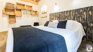 Une chambre avec un grand lit, une tête de lit en bois et des étagères intégrées en bois où sont pliées des serviettes.