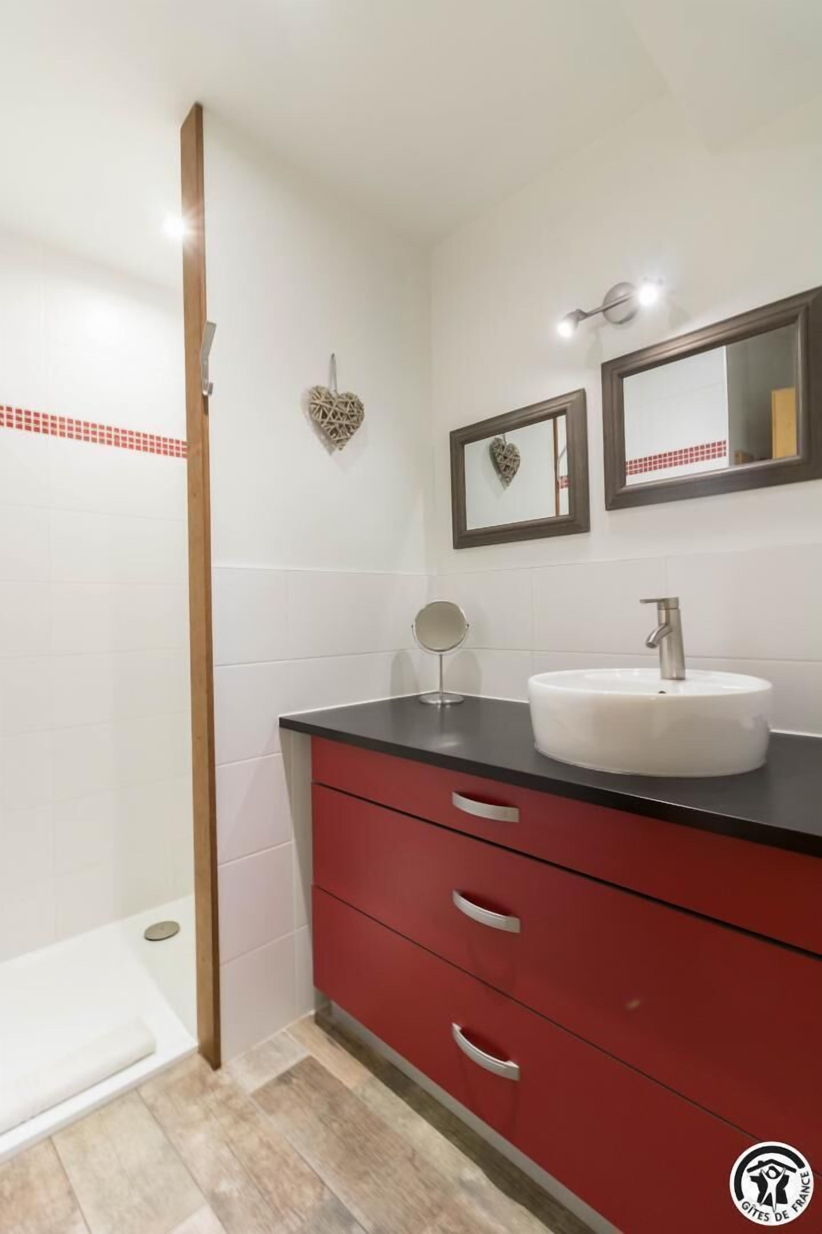 Un bagno con lavandino bianco, mobiletto rosso e zona doccia.