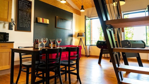 Un coin repas avec une table en bois, des chaises noires et un canapé rouge. Un tableau noir servant de menu est accroché au mur, et une fenêtre offre une vue sur la verdure à l’extérieur.