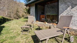Un espacio exterior moderno con mobiliario de mimbre, una pared de piedra y vistas al interior.