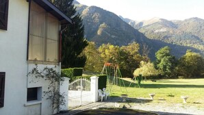 Una casa con fachada blanca, entrada protegida por una reja y un parque infantil en el patio.