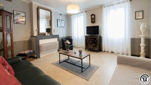 Ein Wohnzimmer mit einer Couch, einem Couchtisch, einem Kamin, einem Fernseher und einer Wanduhr.