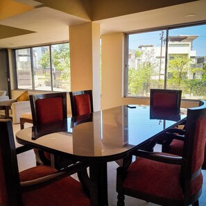 A conference room with a glass table surrounded by red upholstered chairs, large windows offering a view of the outdoors. - Embera by Joy Suites (Mawal)