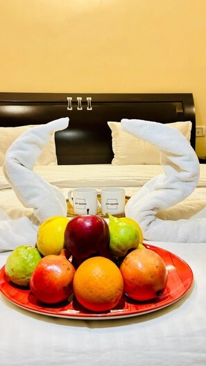A bed with a black headboard, two white towels arranged in a heart shape, and a plate of fruit in front of the bed.