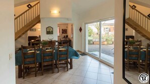 Un espace repas avec des tables et des chaises en bois, un escalier et une vue sur l’extérieur.