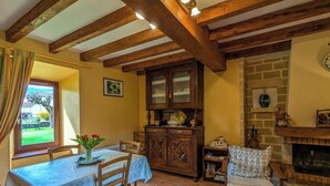 Zona pranzo con tavolo apparecchiato per due, travi in legno al soffitto, camino e parete in mattoni.