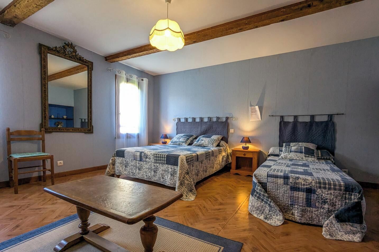 Une chambre avec deux lits, une chaise en bois, une table et un grand miroir.