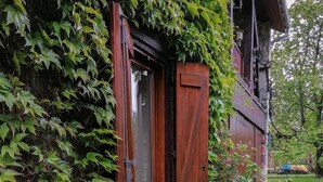 Una casa di legno rustica con una porta e una finestra in legno, circondata da vegetazione lussureggiante e piante fiorite.