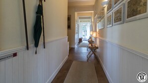 Ein Korridor mit weißer Wandverkleidung, einem Kleiderständer mit einem Mantel und gerahmten Bildern an der Wand.