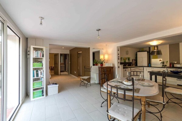 A spacious living area with a dining table, a bookshelf, and a kitchen in the background.