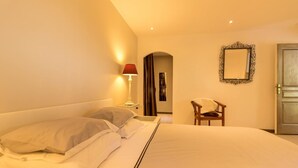 Hotellihuone, jossa on suuri sänky, yöpöytä lampun kanssa, tuoli ja ovi.