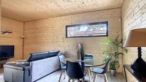 A cozy room with a sofa, a dining table with chairs, a TV, and a window with a view of trees. - L'Oustal de la Mane d'Auta (AYGUESVIVES)