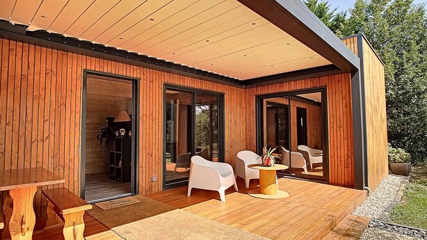 A modern wooden cabin with an open patio, furnished with white chairs and a wooden table. - L'Oustal de la Mane d'Auta (AYGUESVIVES)
