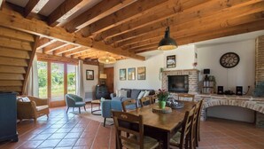 A rustic interior with exposed wooden beams, a fireplace, a dining area, and a living room with a sofa and chairs. - La Ferme de Menoun - Thil (Thil)