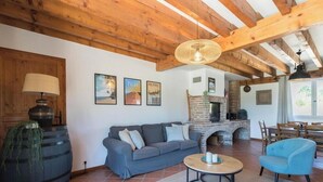 A living room with a sofa, a round coffee table, a blue armchair, a fireplace, wooden beams, and wall art. - La Ferme de Menoun - Thil (Thil)