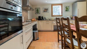 A modern kitchen with stainless steel appliances, a tiled floor, and wooden chairs. - Vignes - Saint-Léon - Gîte (Saint-Léon)