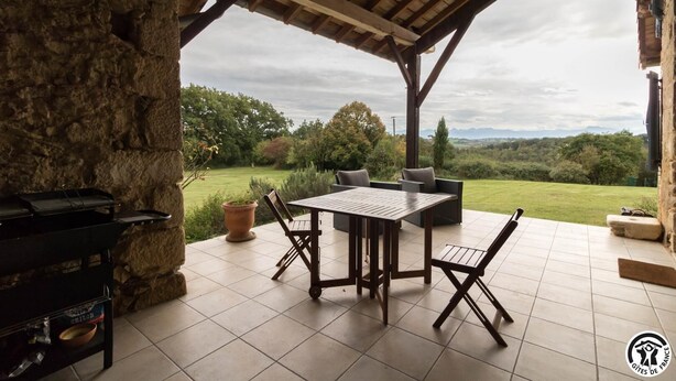 An outdoor patio with a grill, a table with chairs, and a view of a green landscape. - Picanas - Boussan - Gîte (Boussan)