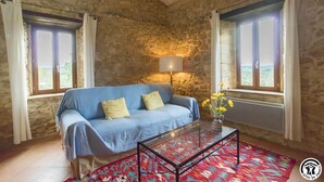 A room with a stone wall, a blue sofa, a glass coffee table, and a patterned rug. - Picanas - Boussan - Gîte (Boussan)