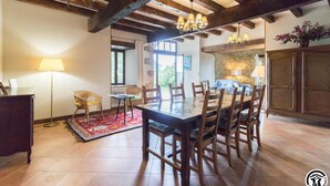 A spacious dining area with a large wooden table and chairs, a chandelier, and a stone wall in the background. - Picanas - Boussan - Gîte (Boussan)