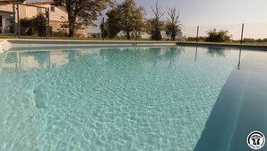 En overskuelig swimmingpool med et afspærret område, træer og en bygning i baggrunden.