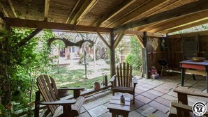 Un espace extérieur abrité, aménagé avec du mobilier en bois, notamment des chaises et une table, et offrant une vue sur le jardin et le bâtiment environnants.