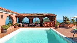 Zona de piscina amb una pèrgola, seients i vista al mar.