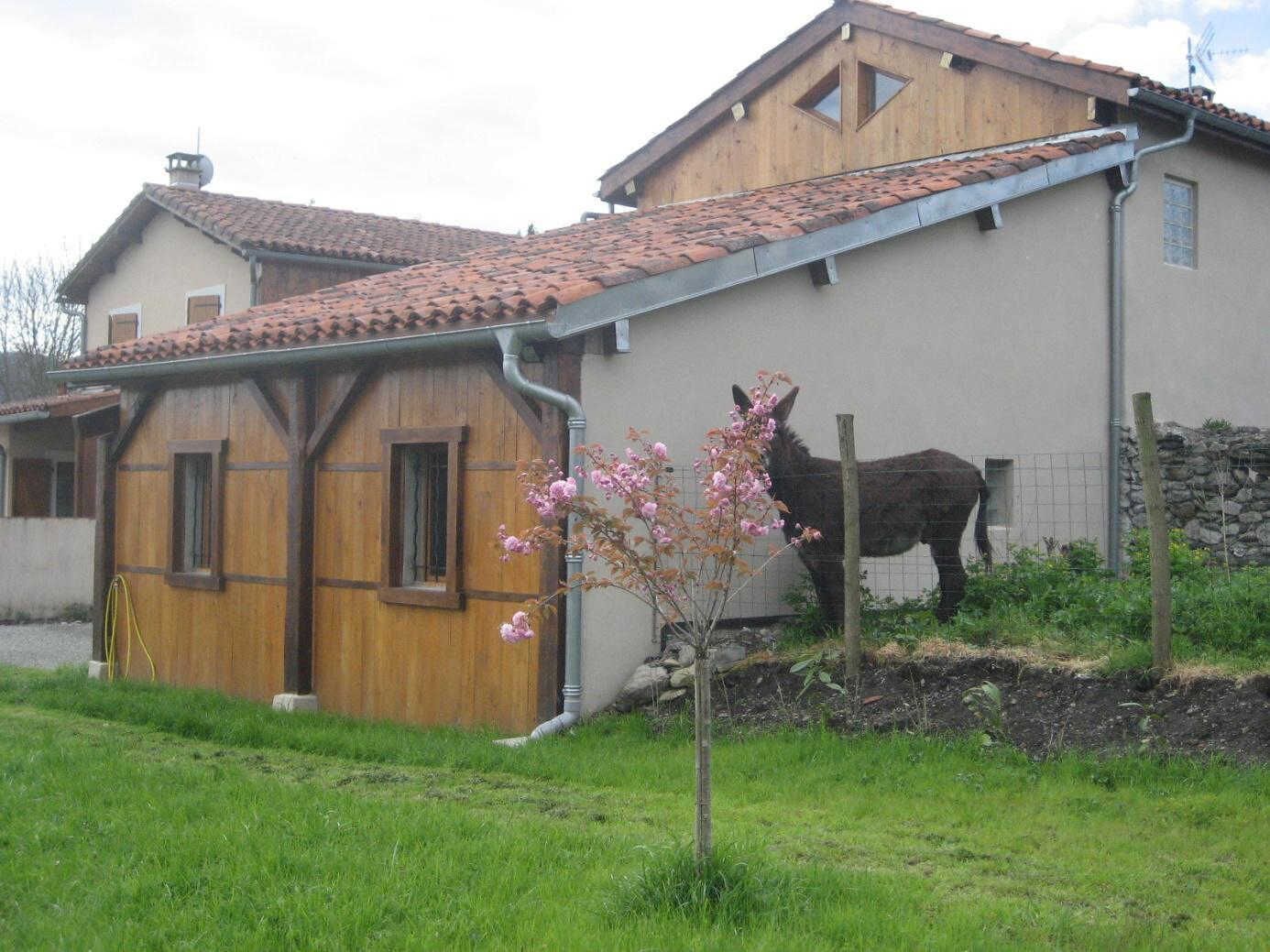 A rustic building with a wooden facade and a tiled roof, adjacent to a fenced area with a horse.