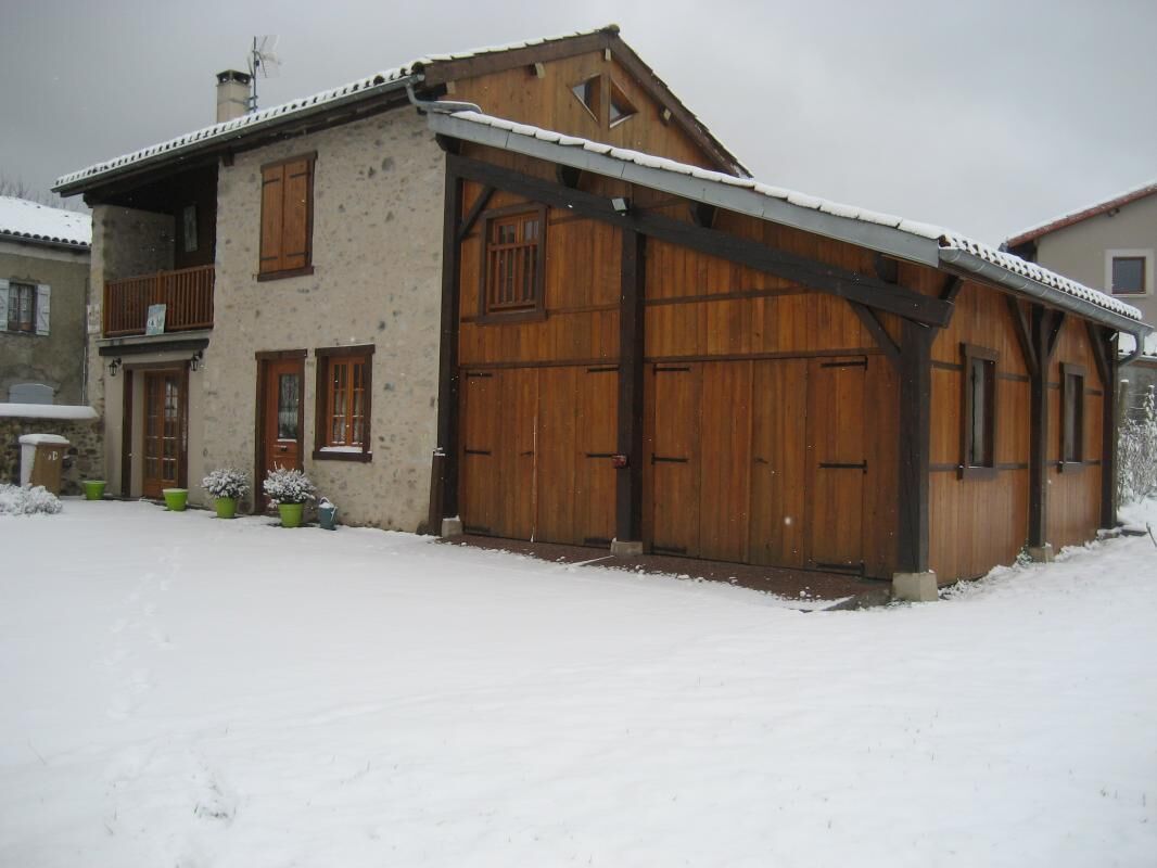 A two-story house with a large wooden garage door, a balcony, and a snow-covered ground.