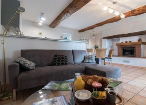 Ein gemütliches Wohnzimmer mit einer Couch, einem Couchtisch mit Frühstücksgebäck, einem Kamin und einer Essecke mit Korbstühlen.