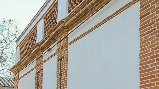 A building with a white facade and red brick accents, featuring a narrow pathway and potted plants.