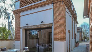 A modern building with a glass door entrance, a patio with chairs, and a small garden area.