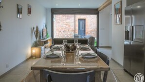 A modern kitchen with a dining table set for four, a large window with a view of a brick building, and a stainless steel refrigerator.