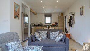 A modern living room with a grey sofa, patterned cushions, and a kitchen in the background.