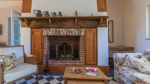 Un salon avec une cheminée en briques, des poutres apparentes, un sol à carreaux et des meubles à motifs floraux.