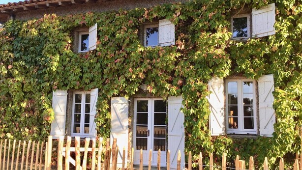 Un bâtiment rustique avec une façade en pierre, des volets en bois aux fenêtres et une clôture en bois à l’avant.